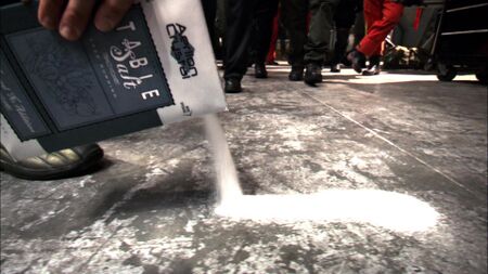 Summary Margaret Edmondson pours a line of Aerilon Crystal table salt down the hangar deck floor as part of a ceremony .