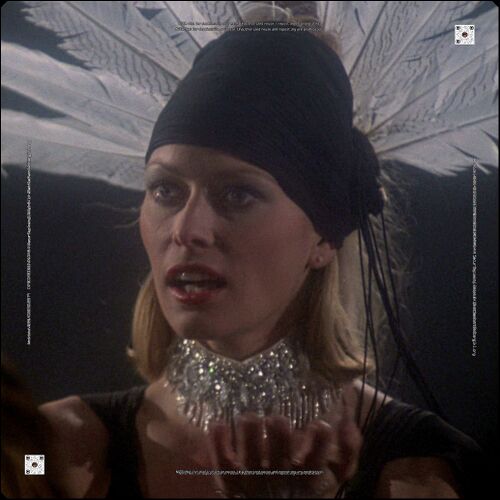 The Blonde Taurus, sporting a black dress with jewelry and a feathered headpiece.